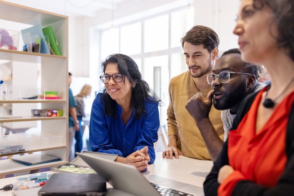 Multiracial businesspeople having meeting in office. Startup business team standing at table with laptop and looking away.