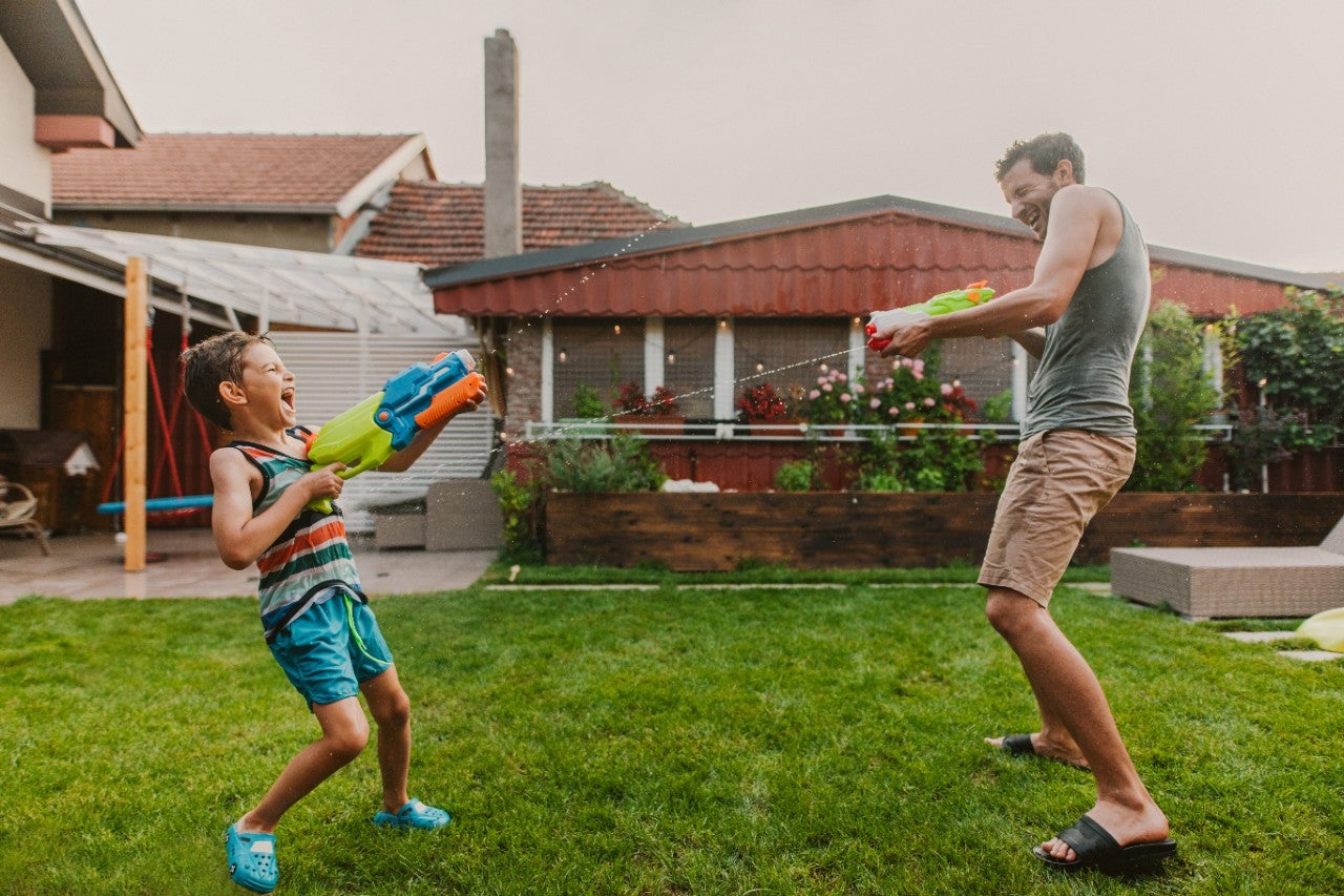 A child and an adult happily playing with water guns in a backyard.