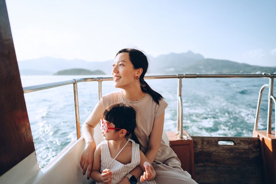 Young Asian mother and lovely little daughter with red sunglasses enjoying a yacht ride over nice calm sea on a summer day. Looking over and relaxed at the sea. Family lifestyle. Enjoying outdoor fun, boat trip and sea vacations