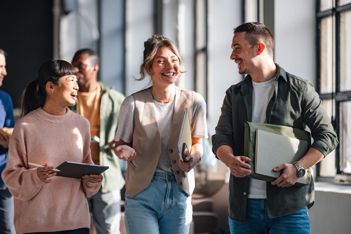 A group of young adults, possibly students or professionals, are conversing and collaborating in a bright, modern co-working environment.