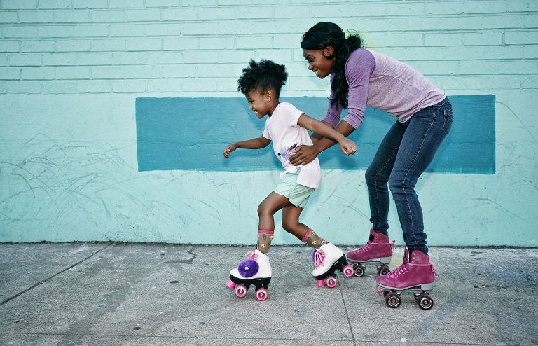 Black mother holding waist of daughter wearing roller skates