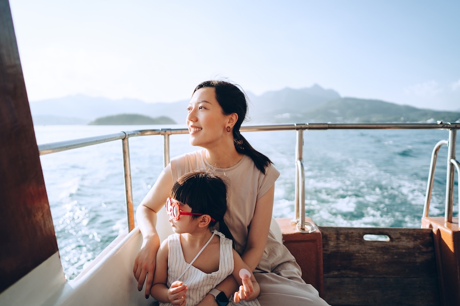 Young Asian mother and lovely little daughter with red sunglasses enjoying a yacht ride over nice calm sea on a summer day. Looking over and relaxed at the sea. Family lifestyle. Enjoying outdoor fun, boat trip and sea vacations