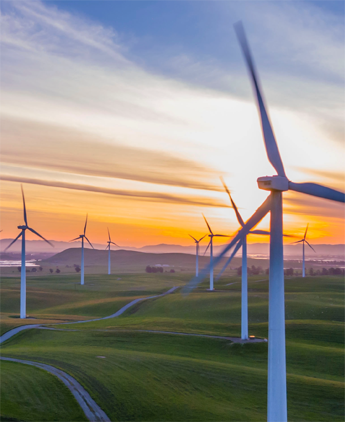 Windmills in a rolling green field at sunset
