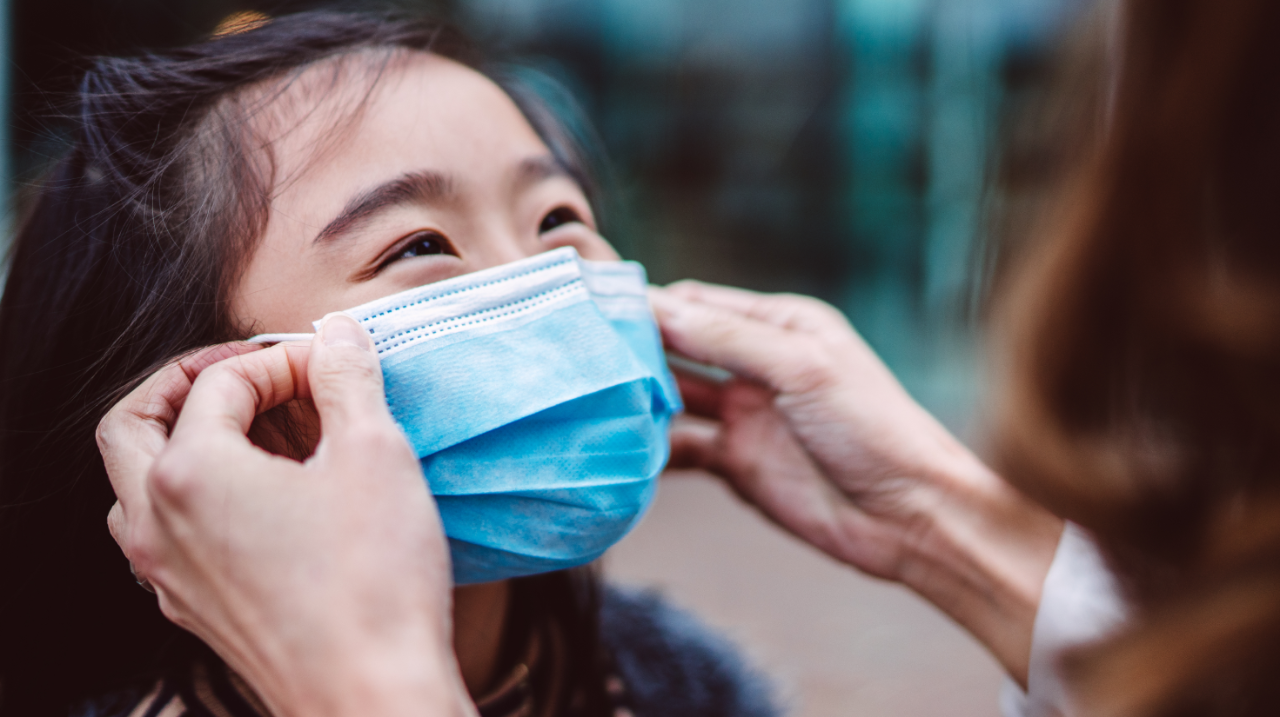 Happy young child getting mask put on face by adult hands