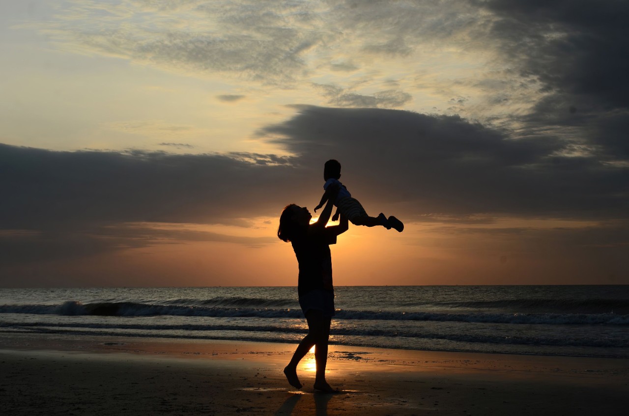 Woman lifting child in front of beach at sunset at Hai Tien Beach, Vietnam